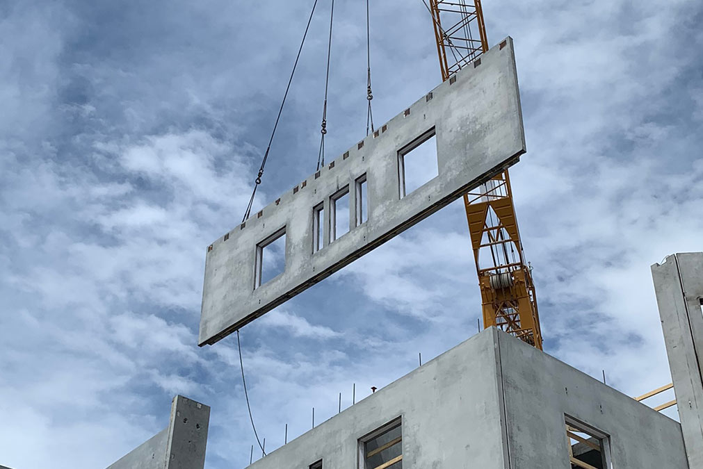A crane installing a large section of precast concrete at a worksite.