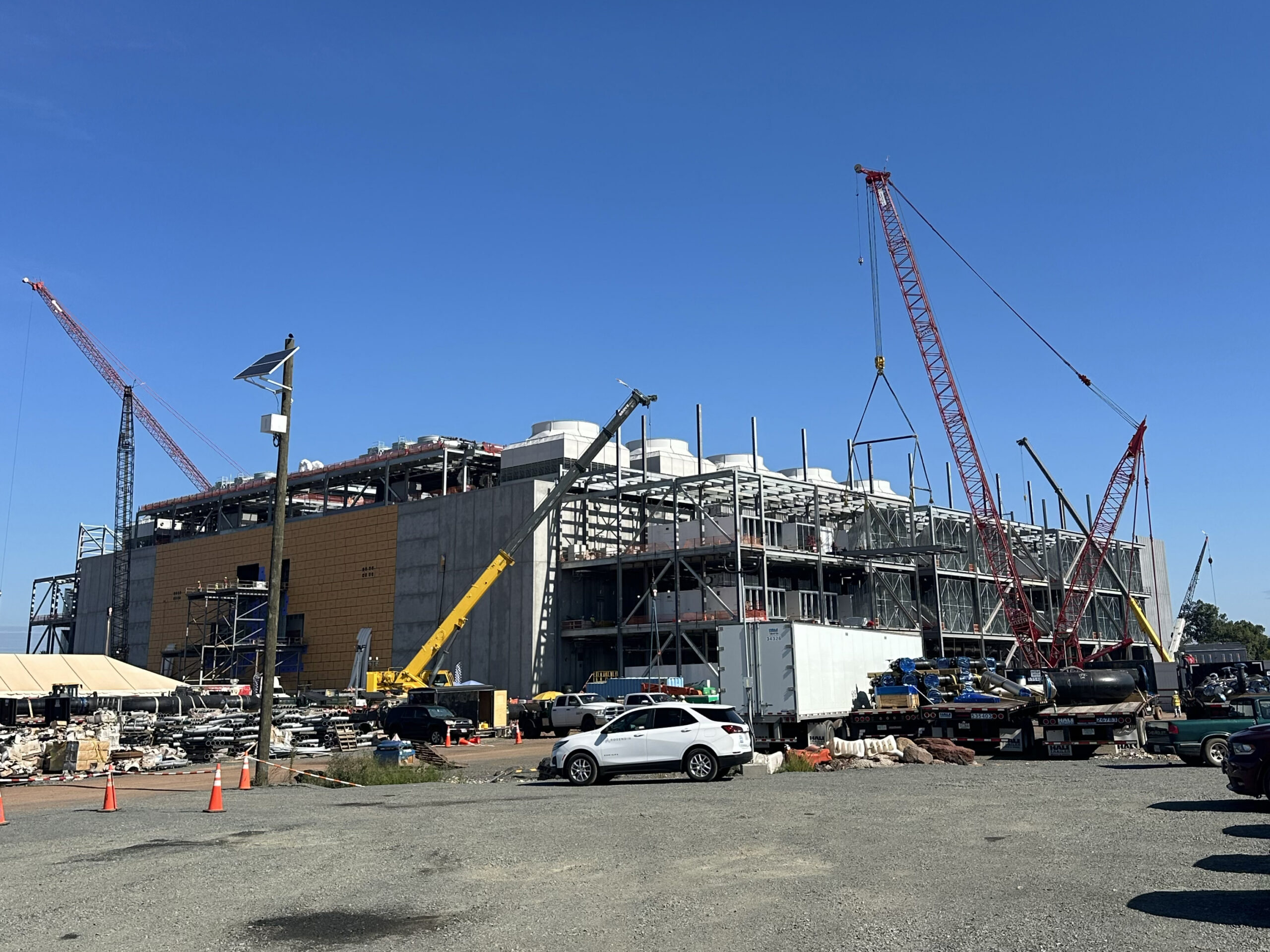 Mission critical facility under construction with cranes, framing, and construction equipment on a clear, sunny day.